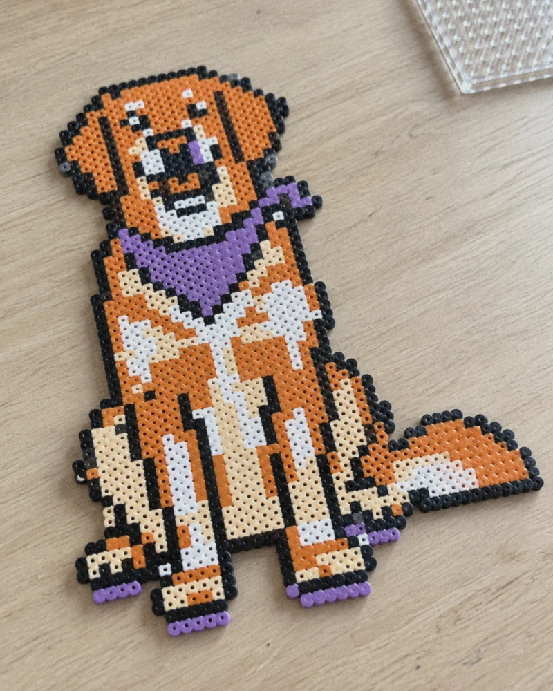 犬の図案をアイロンビーズで作ったときの仕上がりイメージ。木の机に置いたオレンジと黒と紫のビーズ