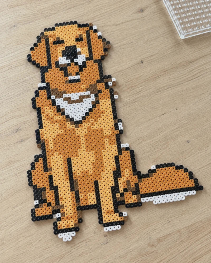 Preview of the dog made with fuse beads in orange, light orange, brown, black and white, on a wooden table